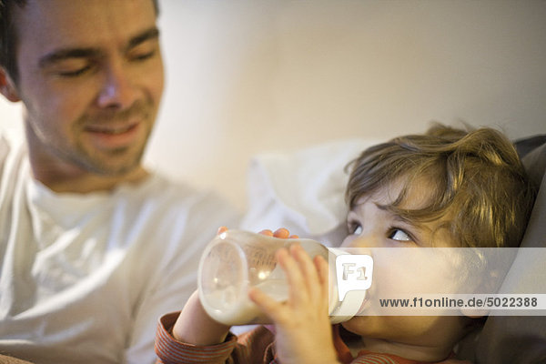 Toddler boy with father  drinking milk from baby bottle