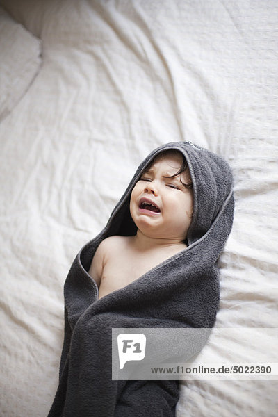 Crying toddler wrapped in a towel after bath
