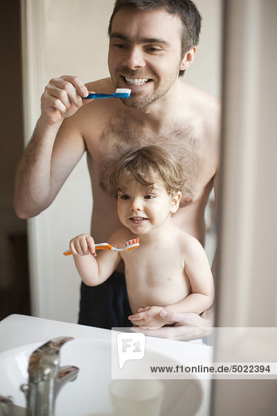 Father and toddler son brushing their teeth together