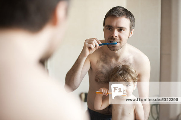 Father and toddler son brushing their teeth together