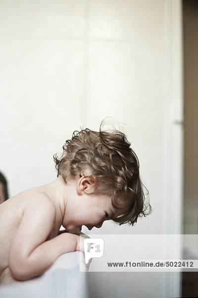 Toddler boy leaning over side of bathtub crying