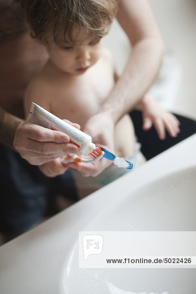 Father helping toddler son brush his teeth