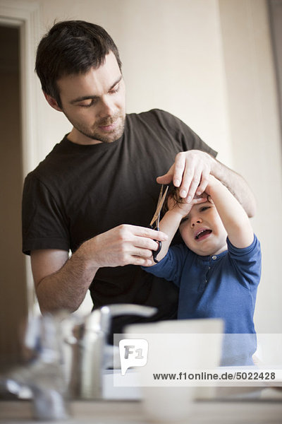 Vater gibt weinendes Kind einen Haarschnitt