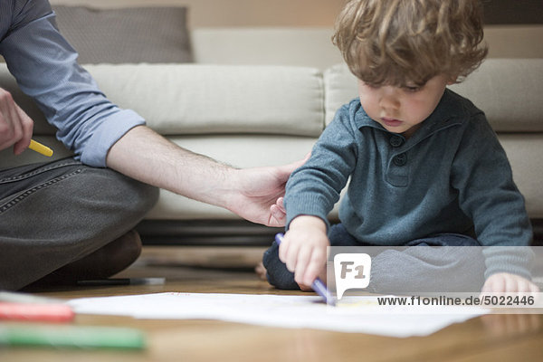 Kleinkind Junge sitzend auf dem Boden mit Vater  Zeichnung auf Papier