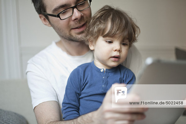 Toddler boy watching father using digital tablet