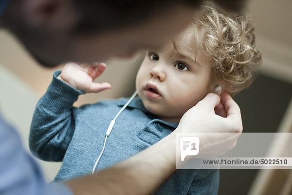 Vater hilft Kleinkind Sohn benutzen Kopfhörer