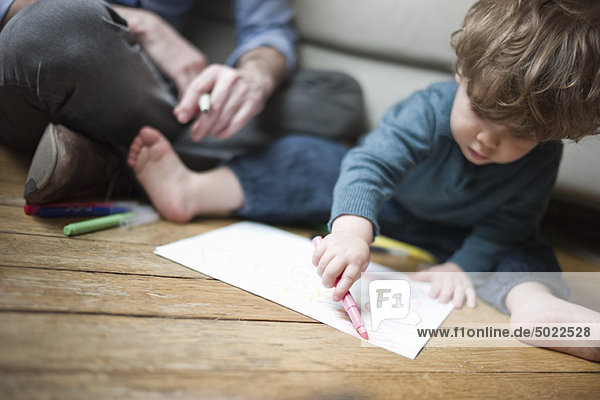 Toddler boy sitting on floor with parent  drawing on paper