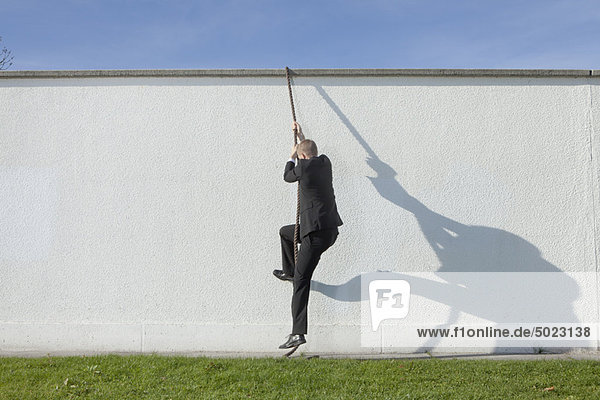 Geschäftsmann klettert mit Seil über die Wand