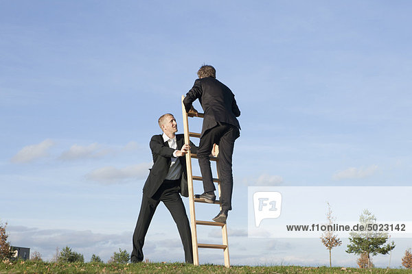 Businessman holding ladder for colleague