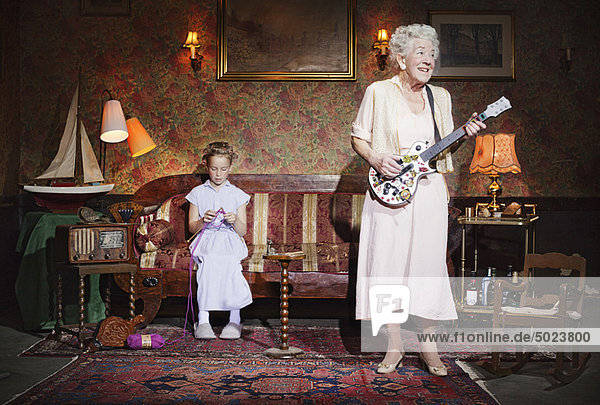Ältere Frau spielt Gitarre als Mädchen strickt
