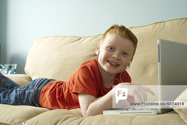 Boy in headphones using laptop on couch