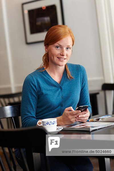 Portrait of young smiling woman in cafe sending message