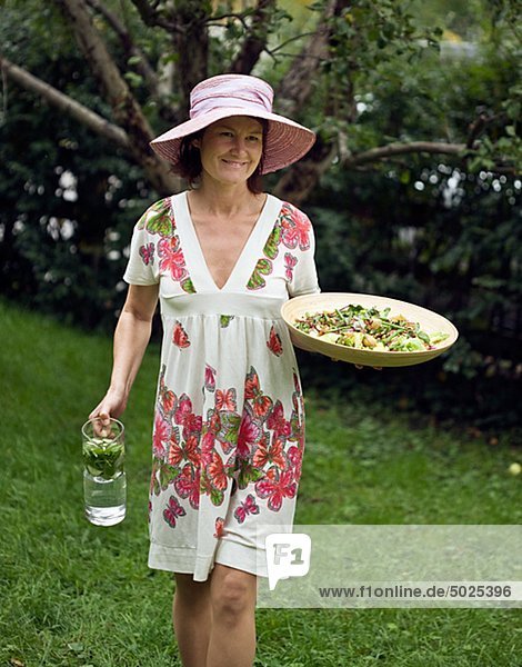 Woman in flowery dress carrying salad and jug of water