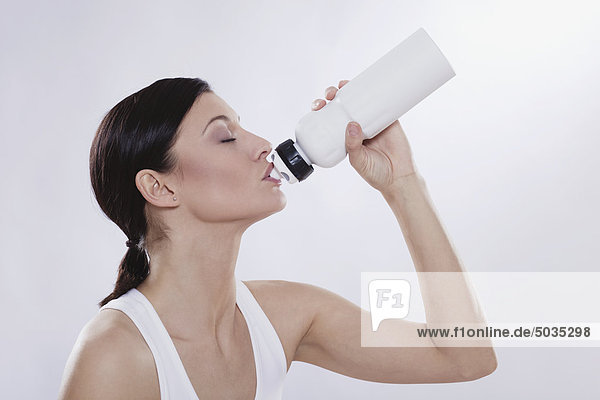 Mittlere erwachsene Frau trinkt aus der Wasserflasche vor weißem Hintergrund