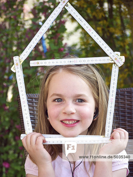 Close up of girl holding house shape made up of folding ruler  smiling  portrait