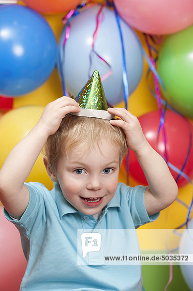 Junge mit Partyhut mit Luftballons im Hintergrund,  lächelnd,  Portrait