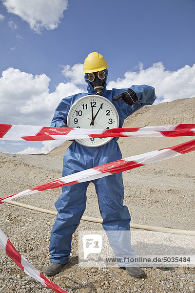 Man in protective wear with clock near sand dune and cordon tape in foreground