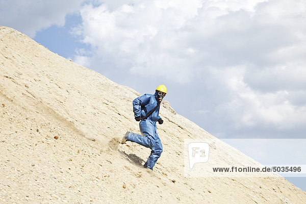 Man in protective workwear running on slope of sand dune