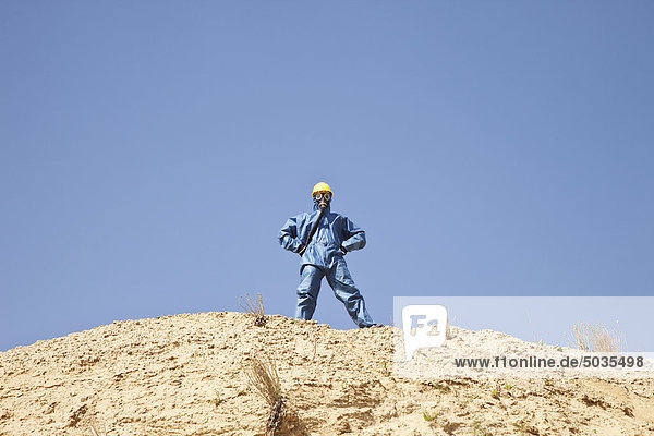 Man in protective workwear standing on top of sand dune