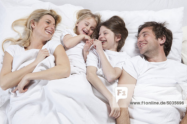 Deutschland  Bayern  München  Familie im Bett liegend  lachend
