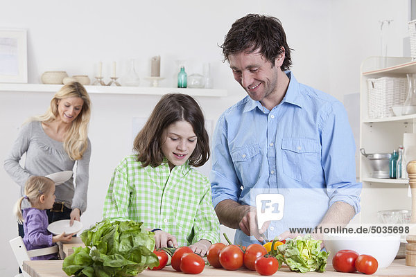 Deutschland  Bayern  München  Sohn bereitet Salat mit Vater  Mutter und Tochter im Hintergrund zu.