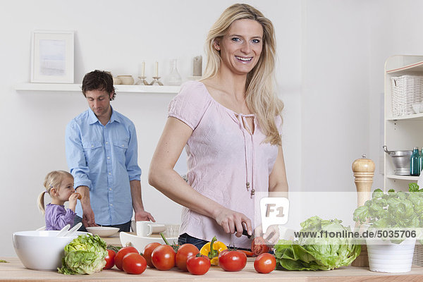 Deutschland  Bayern  München  Mutter bereitet Salat mit Vater und Tochter im Hintergrund zu.