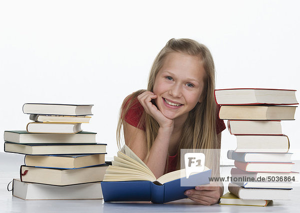 Mädchen hält Buch neben Buchstapel vor weißem Hintergrund  lächelnd  Portrait