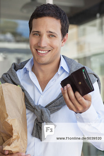 Portrait of a man showing empty wallet with paper bag full of vegetables