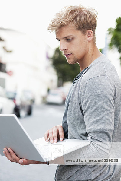 Junger Mann mit einem Laptop auf der Straße