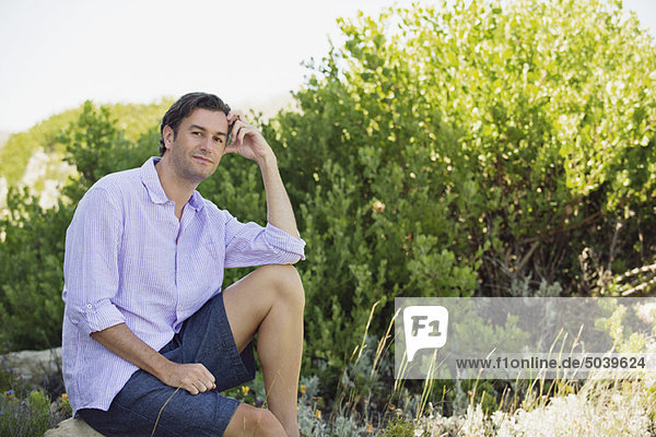 Ein erwachsener Mann  der auf einem Felsen in einem Garten sitzt und nachdenkt.