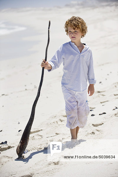 Junge stehend mit einem Holzstab am Strand