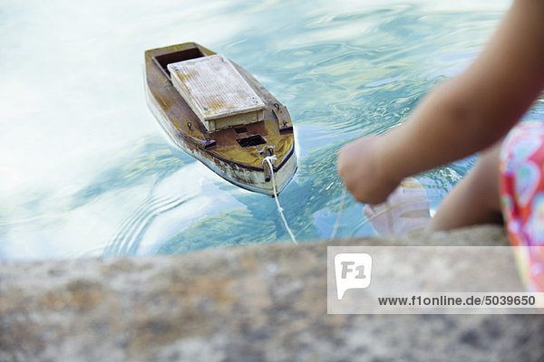 Ansicht eines Mädchens am Rand des Swimmingpools mit Spielzeugboot im Wasser