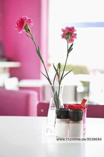 Vase mit rosa Blumen und Salz- und Pfefferstreuer auf einem Tisch im Restaurant