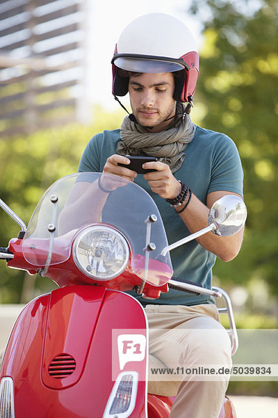 Mann sitzt auf einem Roller und SMS
