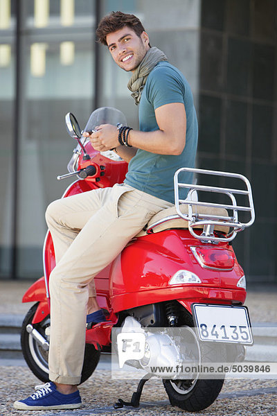 Portrait of young man sitting on a scooter and text messaging