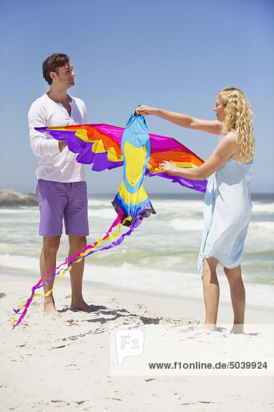 Mittleres erwachsenes Paar  das einen Drachen in Tierform am Strand hält.