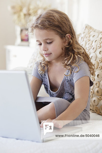 Cute little girl using a laptop in the bed