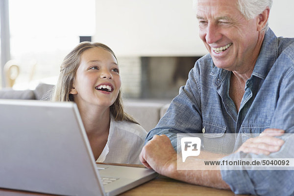 Mann mit seiner Enkelin  der auf einen Laptop schaut und lächelt