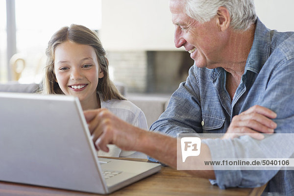 Mann zeigt seiner Enkelin Laptop und lächelt