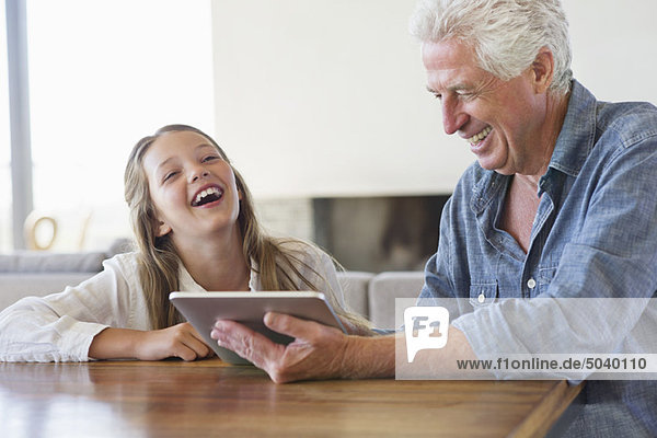 Mädchen lacht  während ihr Großvater ein digitales Tablett benutzt.