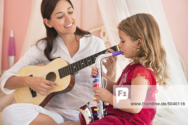 Frau spielt Gitarre mit ihrer Tochter beim Saxophonspielen