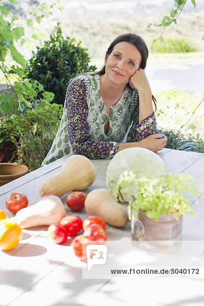 Porträt einer reifen Frau sitzend und Gemüse auf dem Tisch