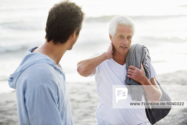Ein älterer Mann spricht mit seinem Sohn am Strand.