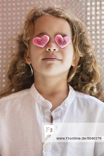 Close-up of a cute little girl covering her eyes with heart shape toys