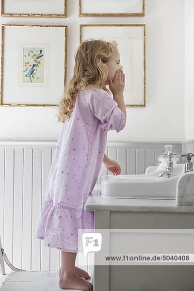 Süßes kleines Mädchen  das sein Gesicht im Badezimmer wäscht.