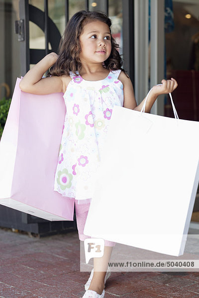 Süßes kleines Mädchen  das aus einem Einkaufszentrum mit Einkaufstaschen kommt.