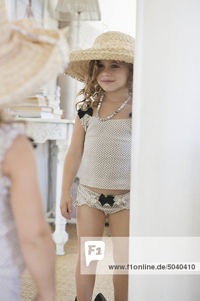 Cute little girl dressed like her mother in oversized accessories and looking at mirror