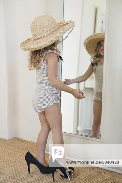 Süßes kleines Mädchen  gekleidet wie ihre Mutter in übergroßen Accessoires und mit Blick auf den Spiegel.