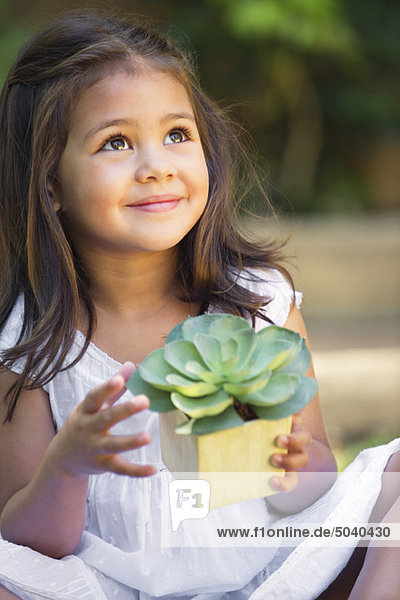 Süßes kleines Mädchen hält eine Topfpflanze und schaut nach oben.