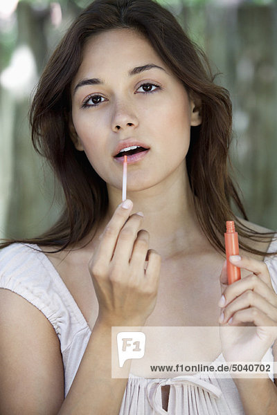 Portrait of a beautiful young woman applying lip gloss